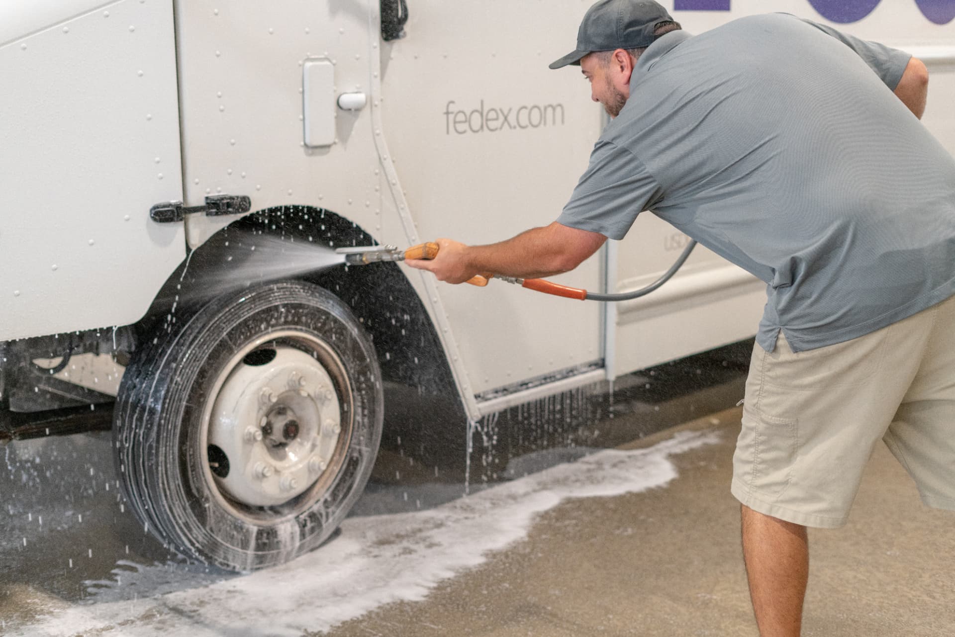 Worker washing the wheel well of a FedEx delivery truck