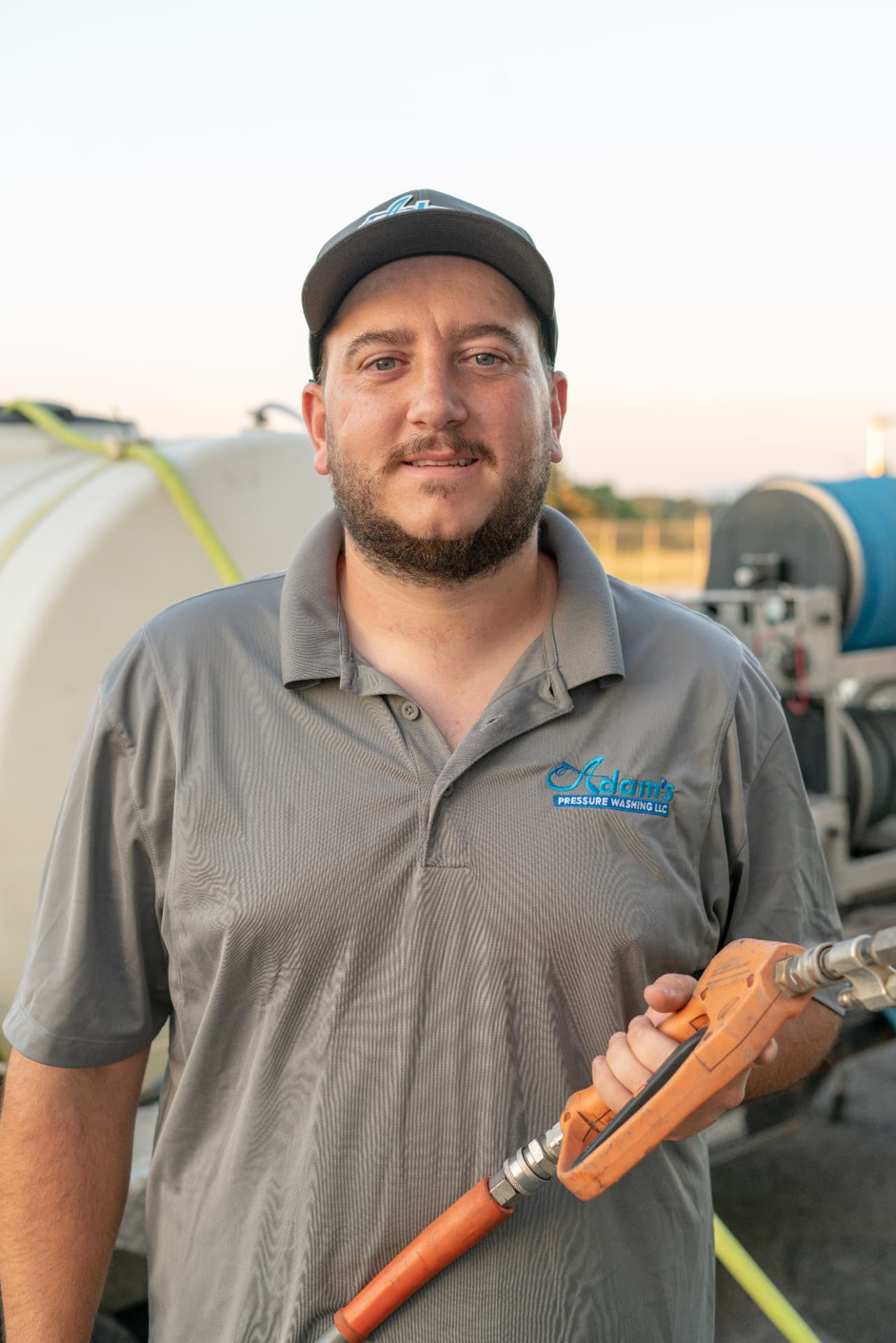 Adam, owner of Adam's Pressure Washing LLC, holding a wash gun beside his rig