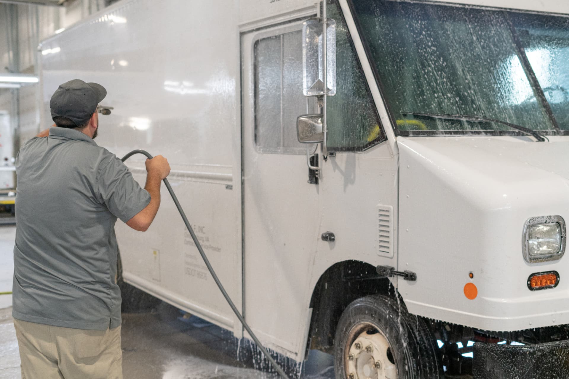 Worker rinsing the full side of a box truck inside a wash bay